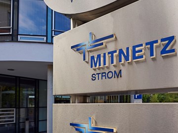 Großes MITNETZ STROM-Logo, blau auf grauem Stahl, am Eingang eines Firmengebäudes Großes MITNETZ STROM-Logo, blau auf grauem Stahl, am Eingang eines Firmengebäudes