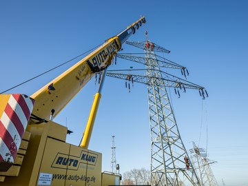 Kran vor einem Hochspannungsmast, in dem mehrere Monteure arbeiten Kran vor einem Hochspannungsmast, in dem mehrere Monteure arbeiten