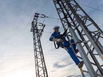 Monteur im Blaumann mit Schutzvisier am Helm sichert sich an einem Hochspannungsmast Monteur im Blaumann mit Schutzvisier am Helm sichert sich an einem Hochspannungsmast