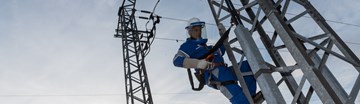 Monteur im Blaumann mit Schutzvisier am Helm sichert sich an einem Hochspannungsmast Monteur im Blaumann mit Schutzvisier am Helm sichert sich an einem Hochspannungsmast