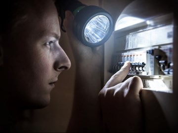 Mann mit Taschenlampe am Stromkasten Mann mit Taschenlampe am Stromkasten