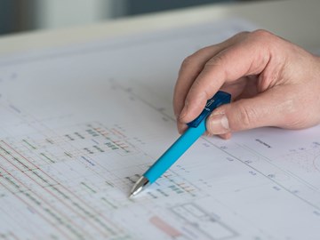 Hand mit Kugelschreiber auf einem Plan - Nahaufnahme Hand mit Kugelschreiber auf einem Plan - Nahaufnahme