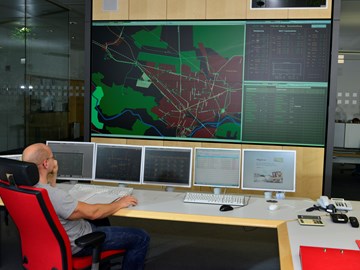 Mitarbeiter auf einem roten Stuhl vor Monitoren mit Schaltleitungen Mitarbeiter auf einem roten Stuhl vor Monitoren mit Schaltleitungen