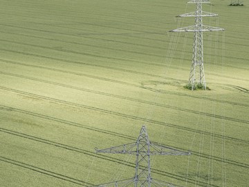 Straße zwischen Feldern über die eine Hochspannungsleitung führt - Luftaufnahme Straße zwischen Feldern über die eine Hochspannungsleitung führt - Luftaufnahme