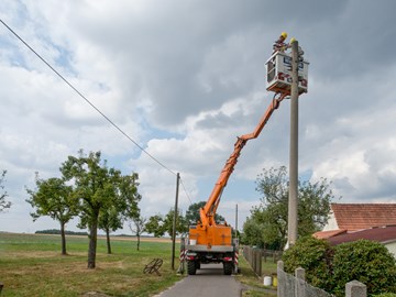 Zwei Arbeiter mit gelben Helmen in der Kanzel eines Krans, an der Spitze eines Strommasts Zwei Arbeiter mit gelben Helmen in der Kanzel eines Krans, an der Spitze eines Strommasts