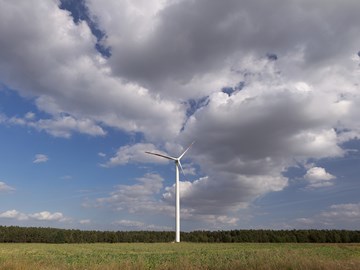 Windrad auf einem grünen Feld vor einem Wald mit wolkigem Himmel Windrad auf einem grünen Feld vor einem Wald mit wolkigem Himmel